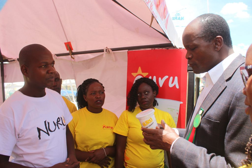 People from Nuru Kenya watching as the governor tastes Nuru yogurt