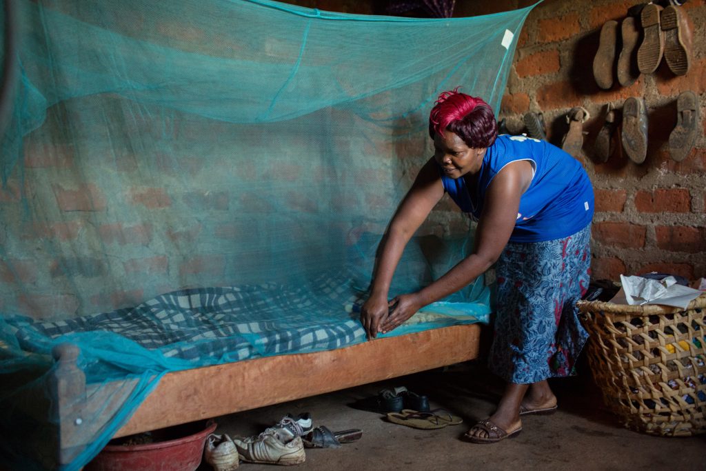 woman tucking in a mosquito net over a bed