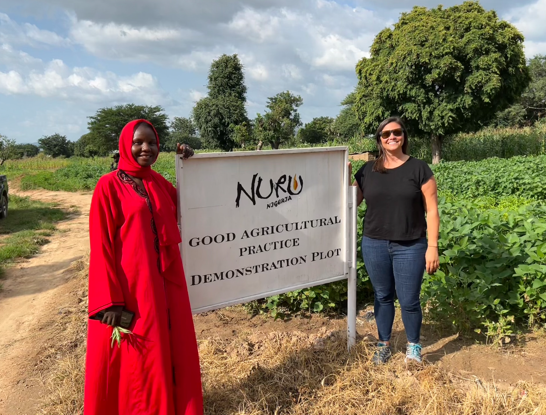 two women standing together by a Nuru Nigeria demo plot sign