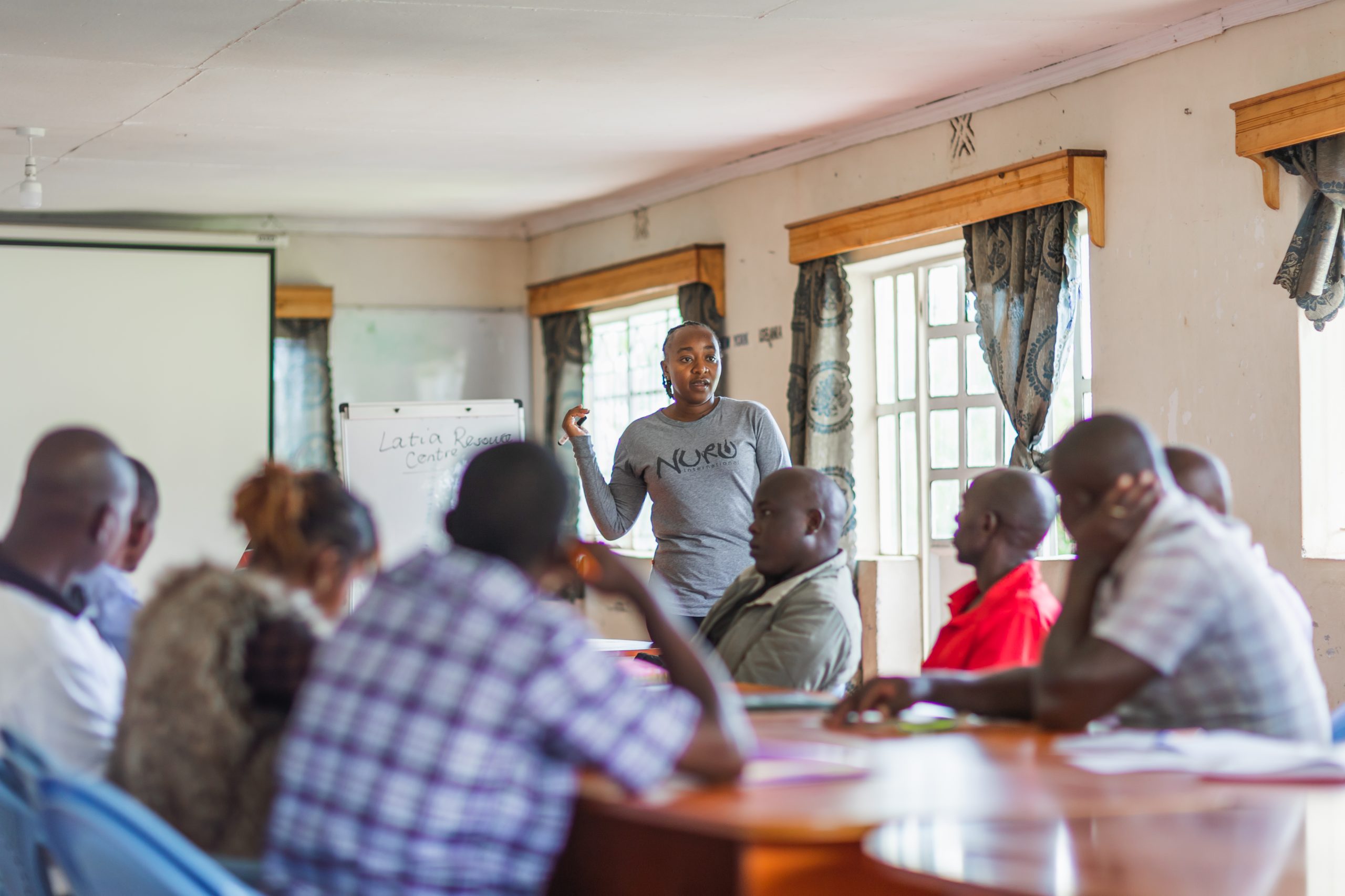 group of people in Kenya gathered around a table a whiteboard for a meeting 