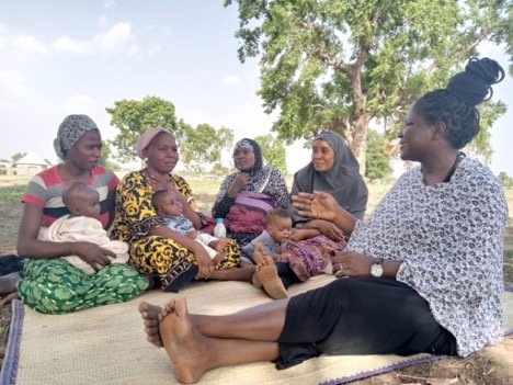 woman in Nigeria sits with fellow women who are holding children