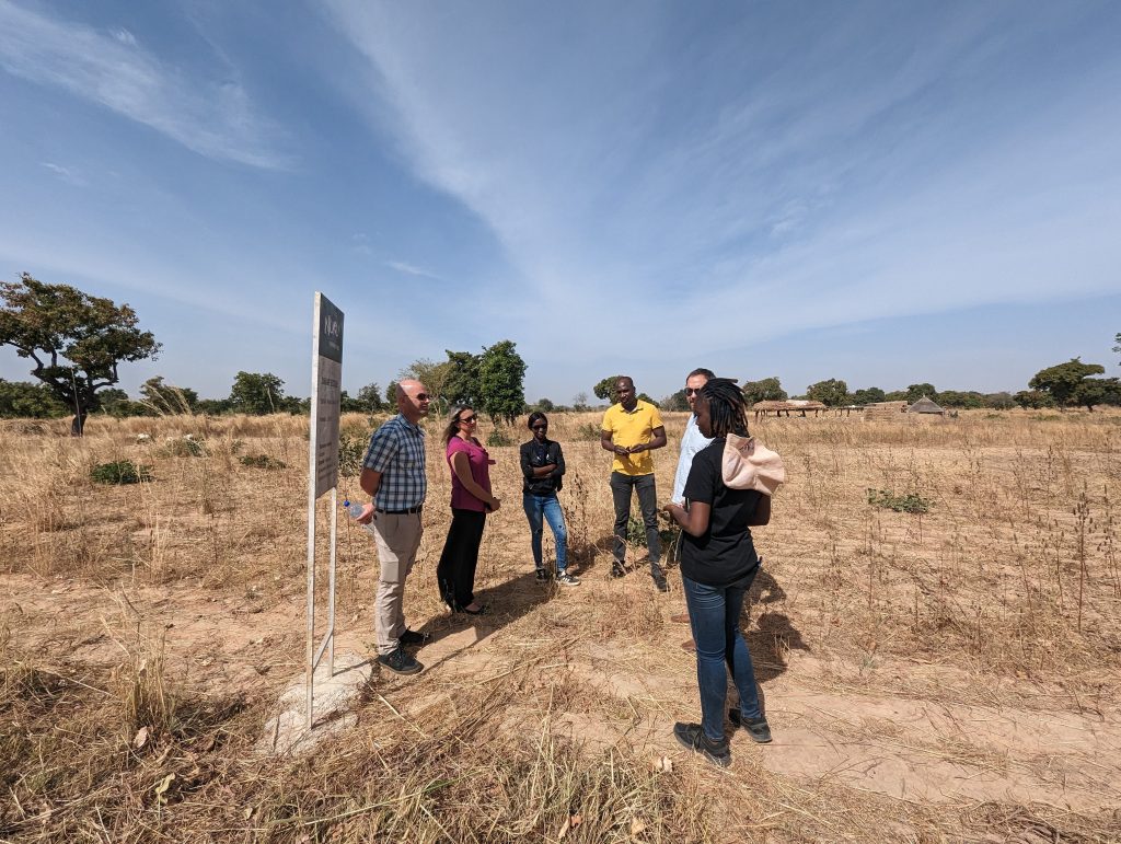 staff from Helmsley Charitable Trust, Nuru International, and Nuru Burkina Faso stand together beside a Nuru Burkina Faso sign