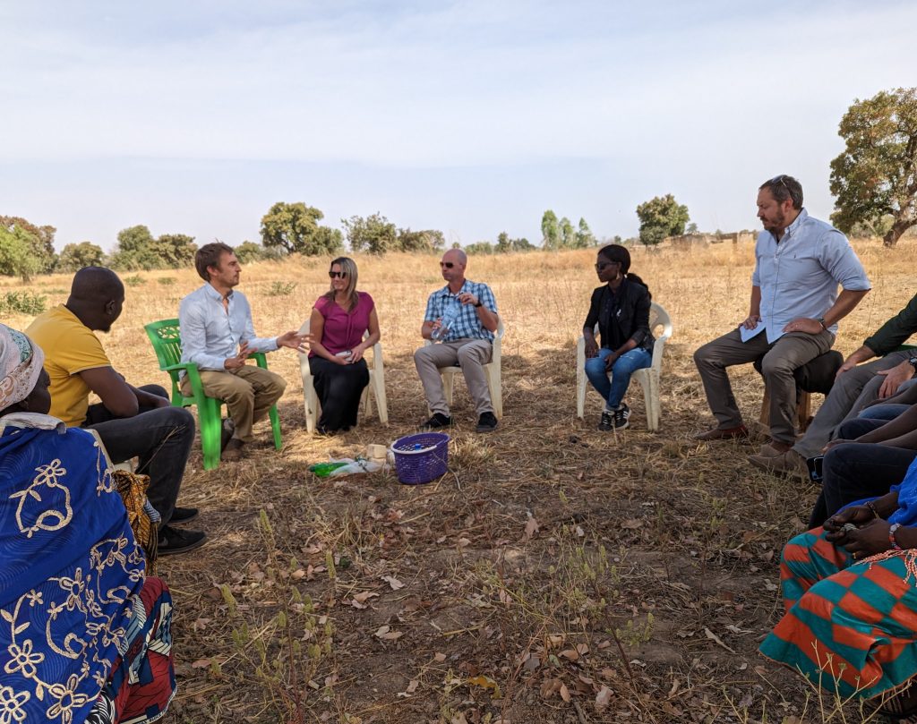 Staff from Helmsley Charitable Trust, Nuru International, and Nuru Burkina Faso sit together in a circle with local community members in Burkina Faso 