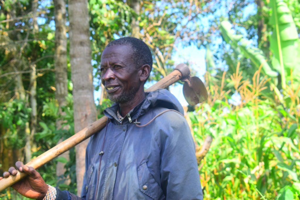 man standing in front of plants and smiling with farming tool (Kenya)