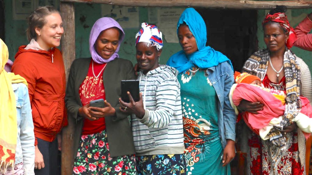 group of women gather together outside and look at phones in Ethiopia