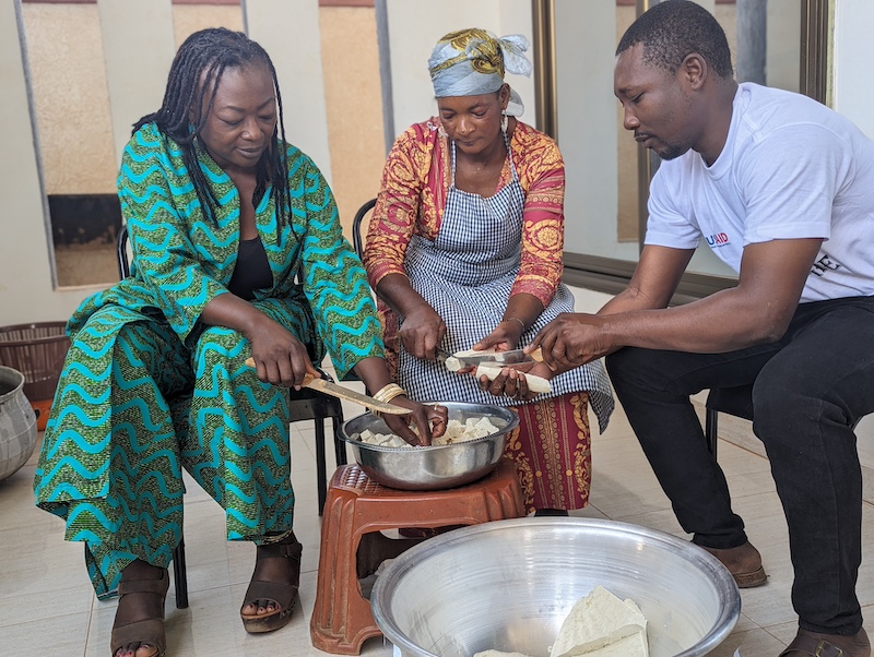 three people gathered around uncooked tofu, cutting the tofu into pieces 