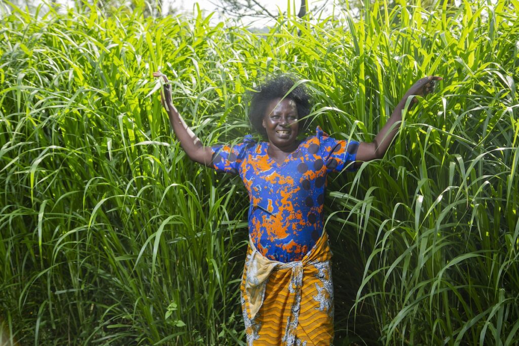 woman in Migori County standing in front of thriving crops and smiling at the camera