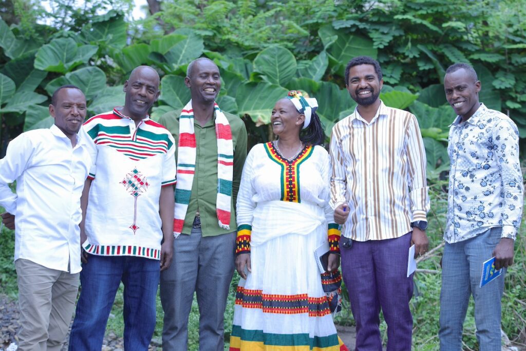 group of people standing together in a line outside, smiling at the camera and one another