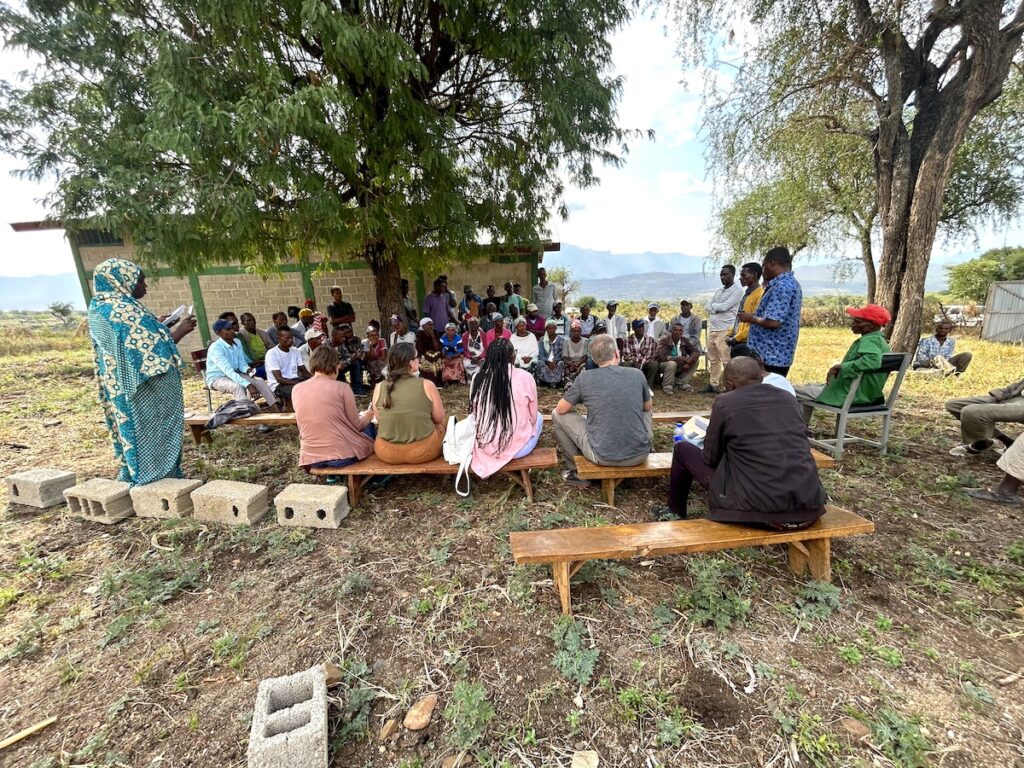 group of people gathered outside on benches underneath a tree in rural Ethiopia