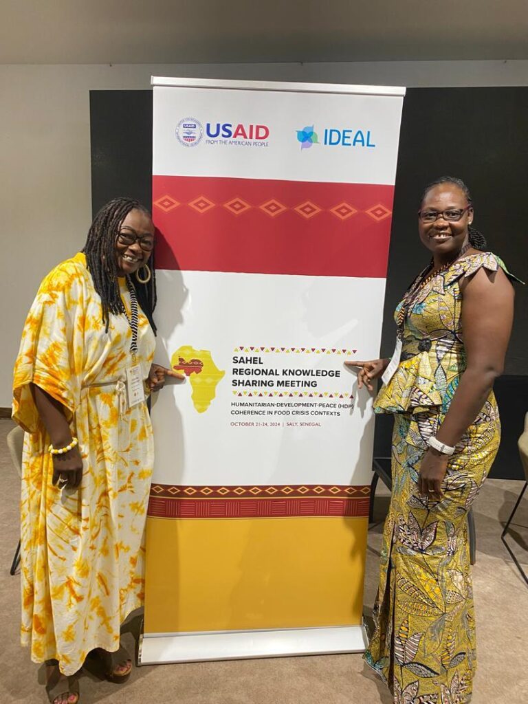 two women standing in front of conference sign together and smiling at the camera